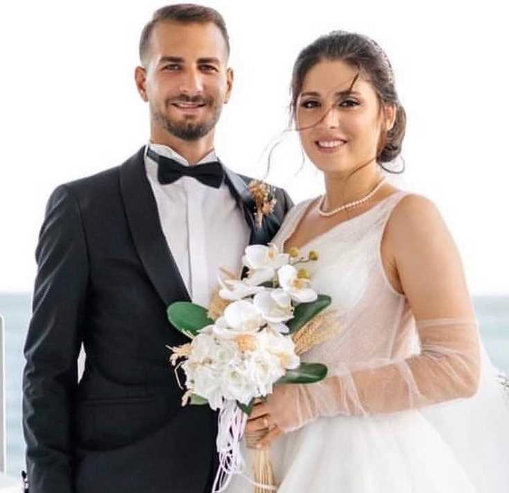 Beyaz çiçekli gelin buketiyle yan yana poz veren gelin ve damat